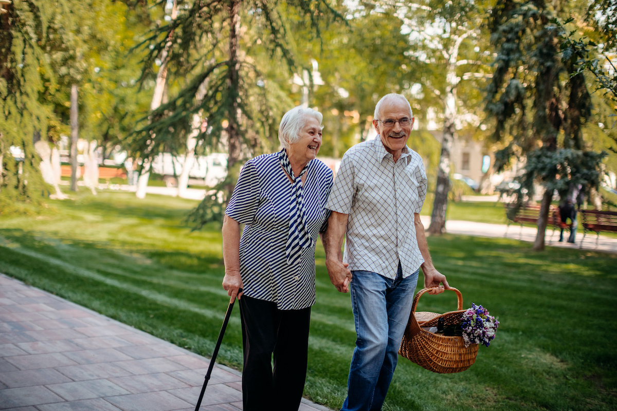 an older couple walking down a sidewalk holding hands and a basket of flowers